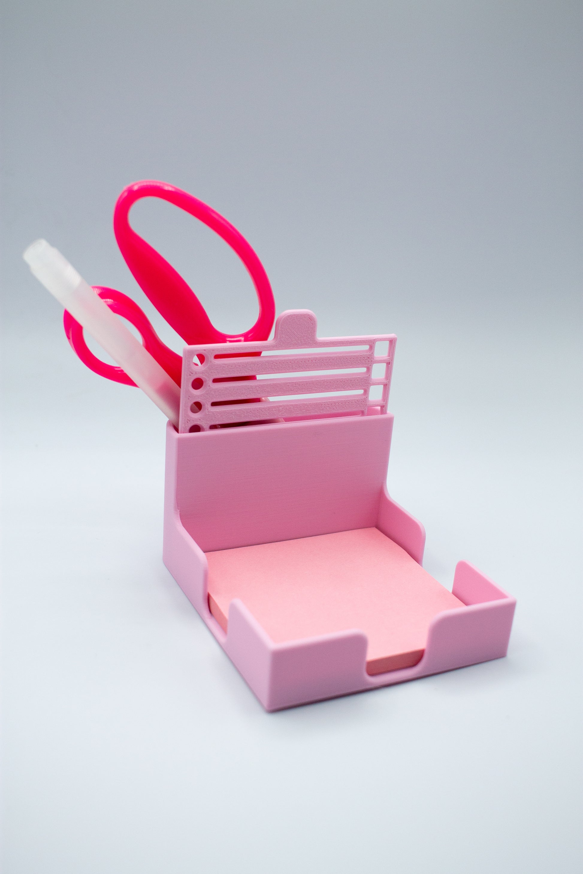Pink post-it holder with to-do list stencil on a light gray background holding pen and scissors